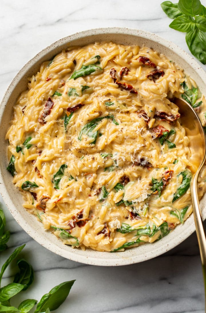 close-up of creamy Tuscan orzo in a serving bowl with a golden spoon and fresh basil leaves
