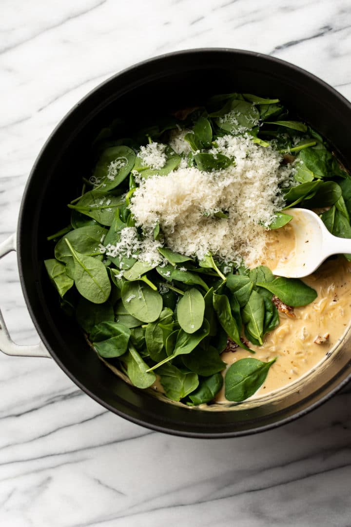 creamy Tuscan orzo close-up of spinach and parmesan being stirred into the pot