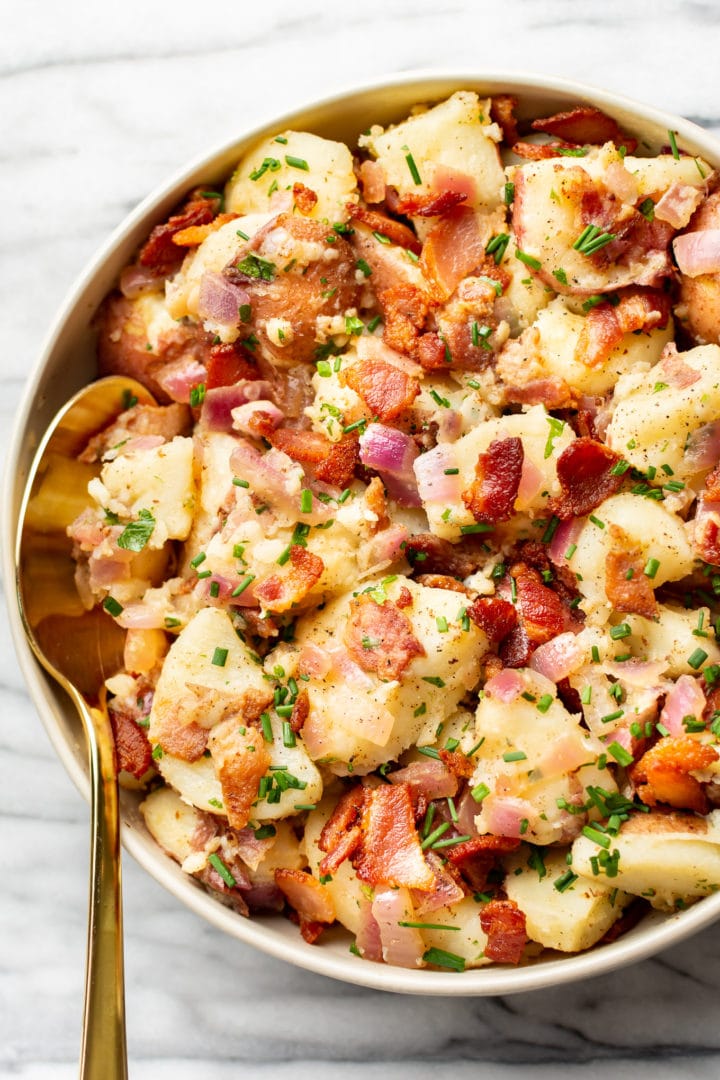 warm German potato salad in a serving bowl with a golden spoon