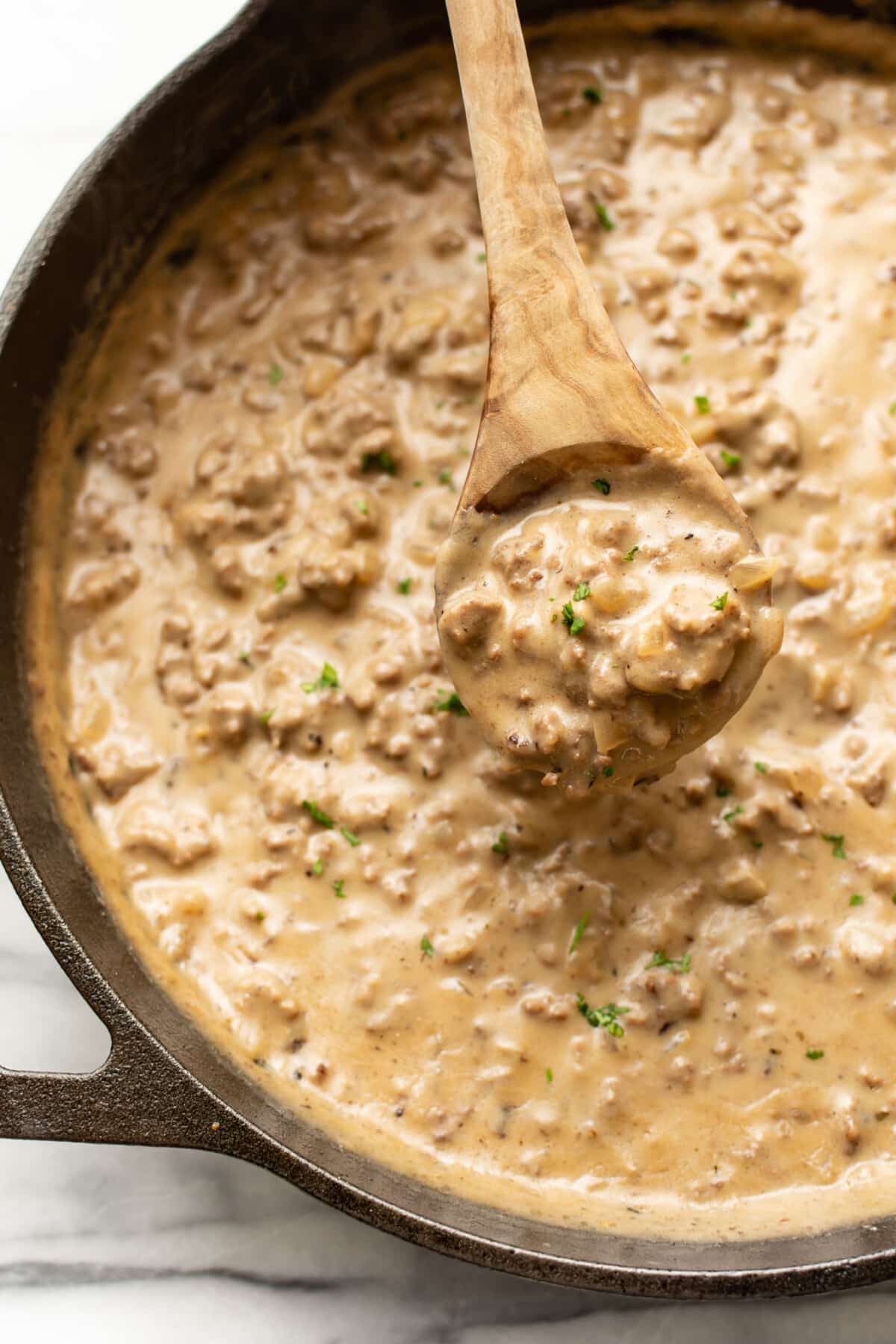 closeup of a skillet of hamburger gravy with a serving spoon