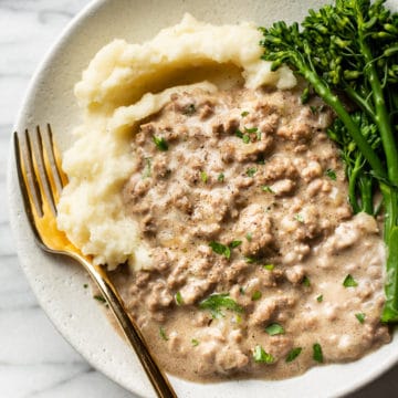 creamed hamburger gravy in a shallow bowl with mashed potatoes and broccolini