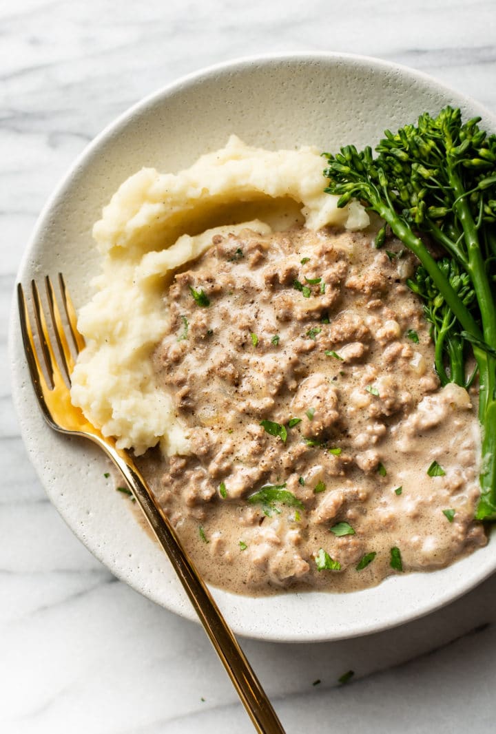 creamed hamburger gravy in a shallow bowl with mashed potatoes and broccolini