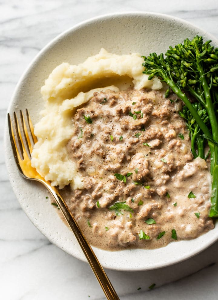 creamed hamburger gravy in a shallow bowl with mashed potatoes and broccolini