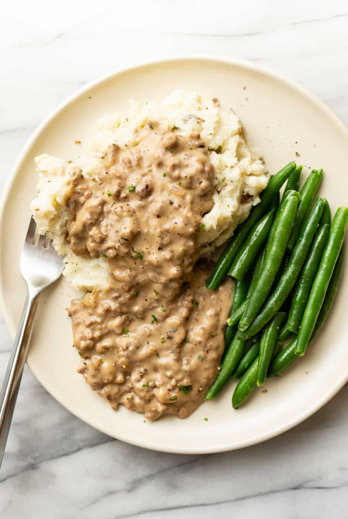 a plate with hamburger gravy, green beans, and mashed potatoes