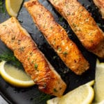 pan seared salmon on a black plate surrounded by lemon wedges