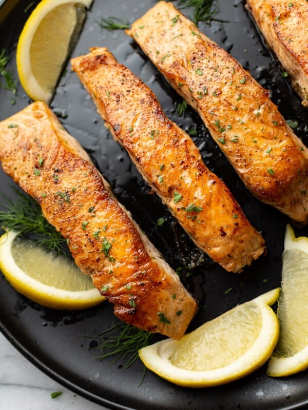 pan seared salmon on a black plate surrounded by lemon wedges