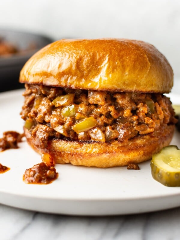 close-up of homemade Sloppy Joe sandwich on a white plate with pickles
