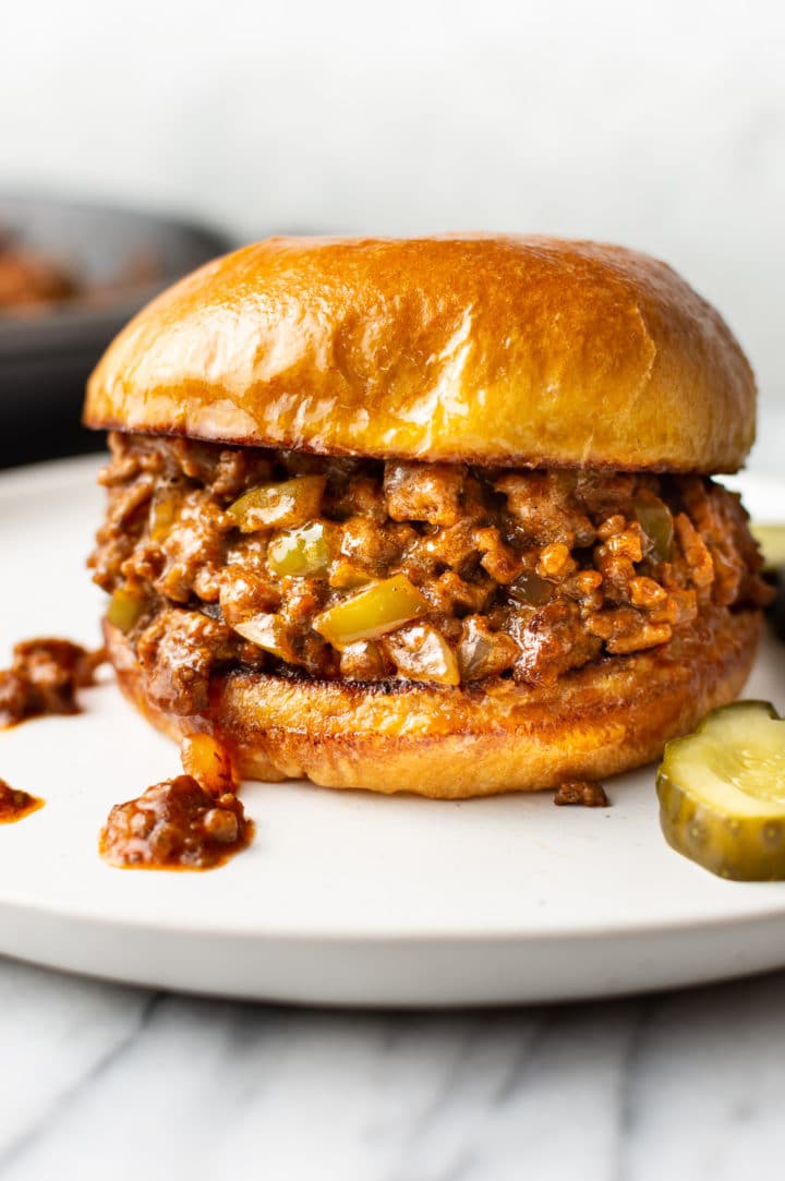 close-up of homemade Sloppy Joe sandwich on a white plate with pickles