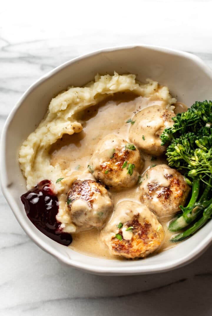 a bowl with mashed potatoes, broccolini, lingonberry sauce, and swedish meatballs