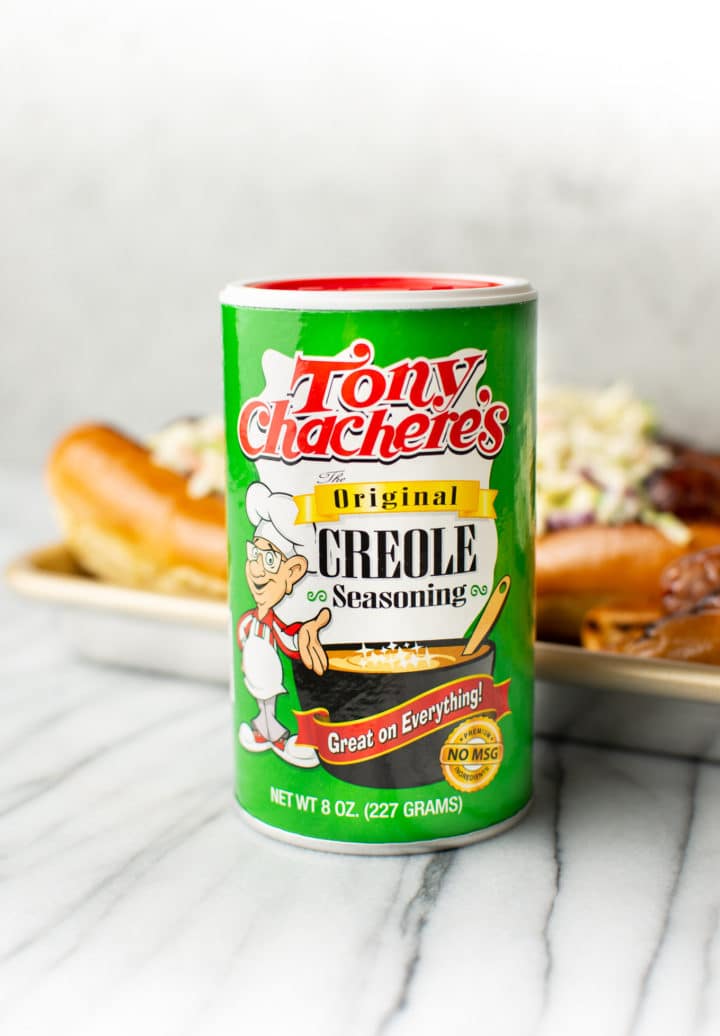 Tony Chachere's Original Creole Seasoning in foreground with a tray of Cajun beer brats in the background