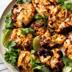 grilled cilantro lime chicken thighs on a plate with lime wedges and fresh cilantro