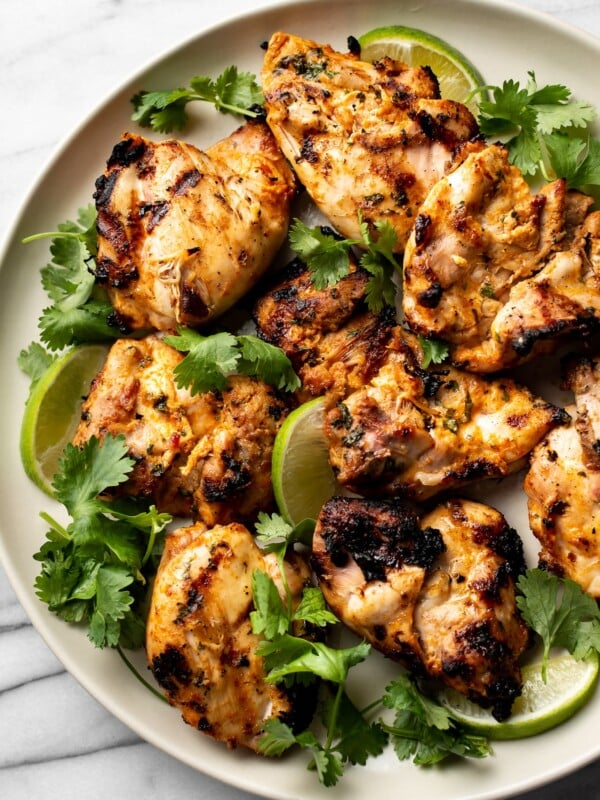 grilled cilantro lime chicken thighs on a plate with lime wedges and fresh cilantro