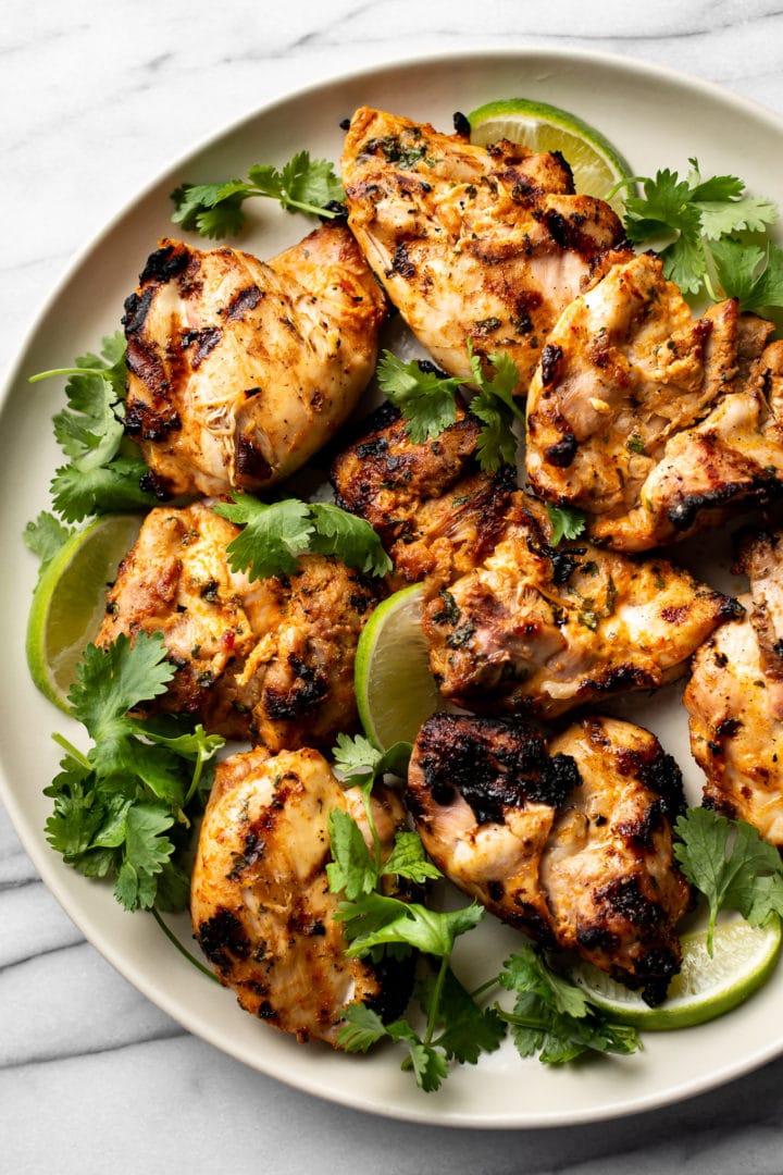 grilled cilantro lime chicken thighs on a plate with lime wedges and fresh cilantro