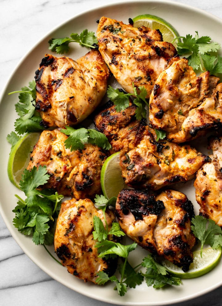 grilled cilantro lime chicken thighs on a plate with lime wedges and fresh cilantro