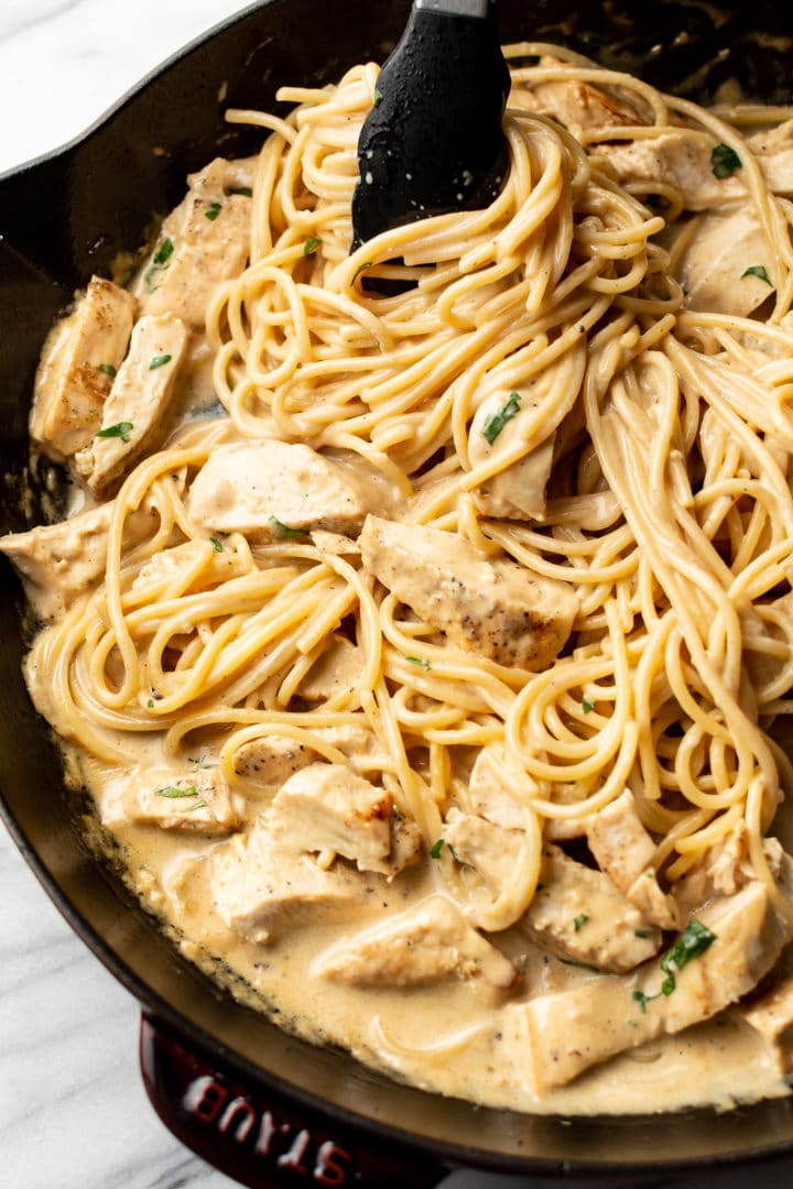 garlic chicken pasta in a skillet being tossed with tongs