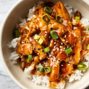 honey garlic slow cooker chicken thighs in a bowl, served over rice and topped with scallions and sesame seeds
