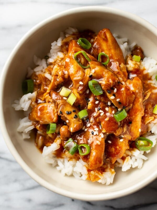 honey garlic slow cooker chicken thighs in a bowl, served over rice and topped with scallions and sesame seeds