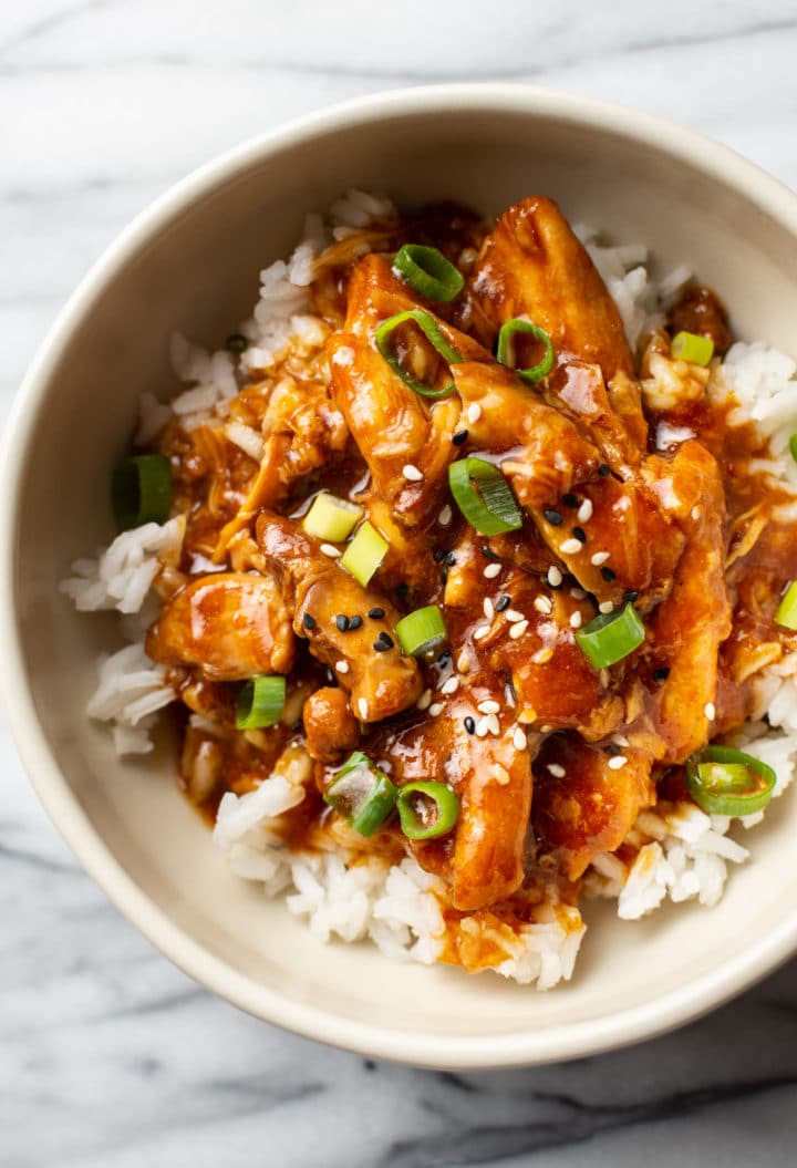 honey garlic slow cooker chicken thighs in a bowl, served over rice and topped with scallions and sesame seeds