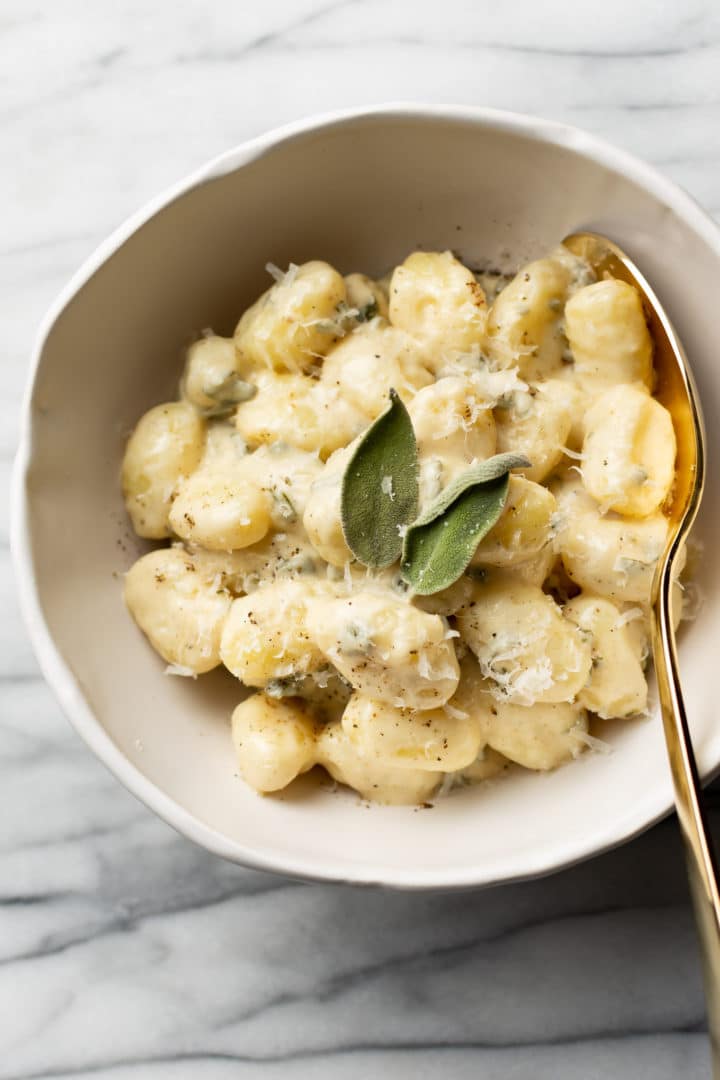 creamy sage gnocchi side dish in a white bowl with a golden serving spoon
