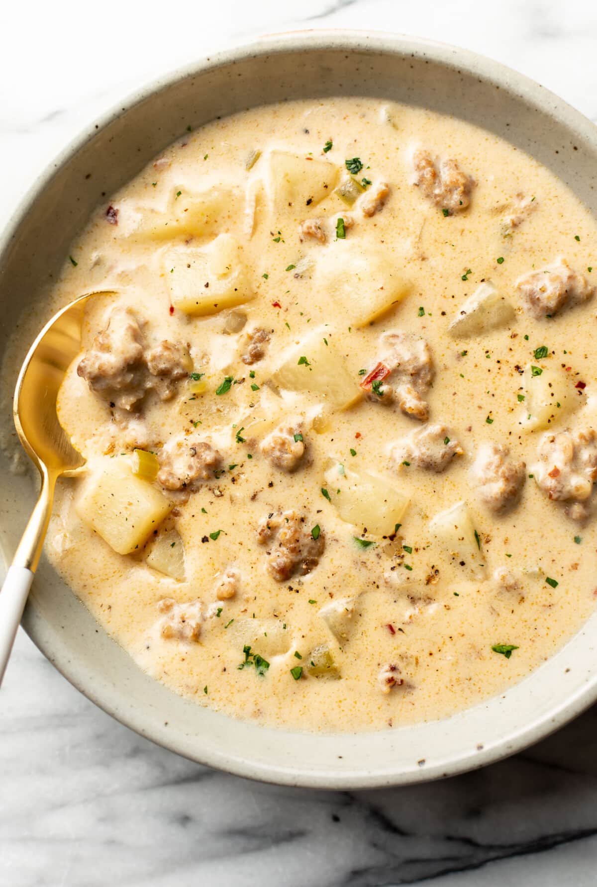 a bowl of creamy sausage and potato soup with a spoon