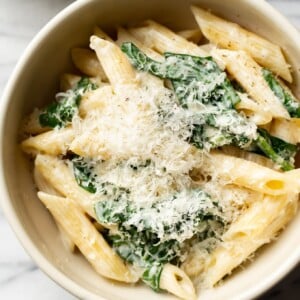 close-up of creamy spinach pasta in a beige bowl