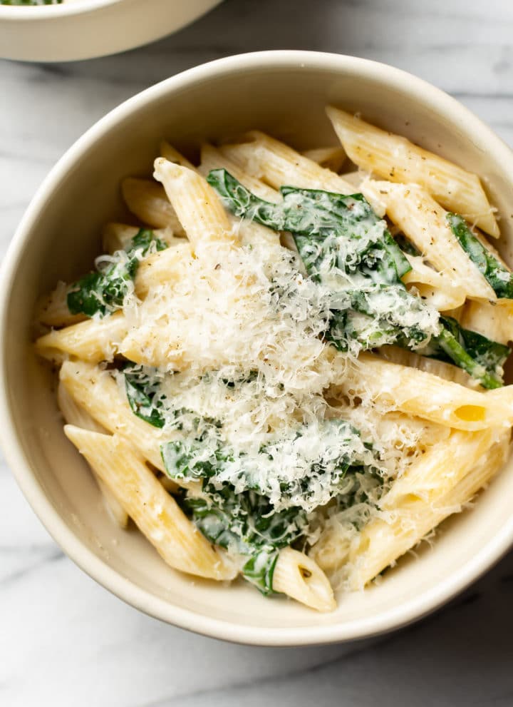close-up of creamy spinach pasta in a beige bowl
