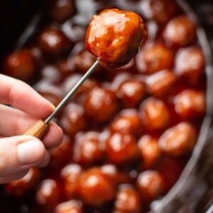 grape jelly meatball being held up on a cocktail toothpick