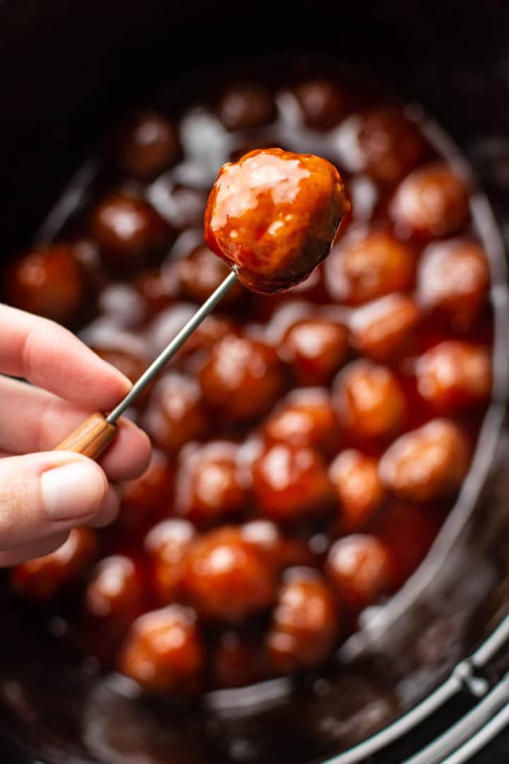 grape jelly meatball being held up on a cocktail toothpick