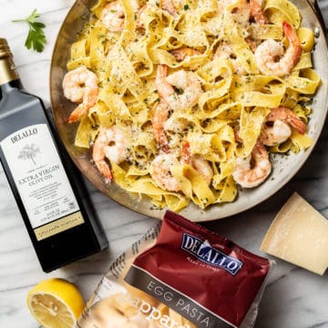 pappardelle with shrimp surrounded by a package of DeLallo's Egg Pappardelle and Private Reserve Olive Oil