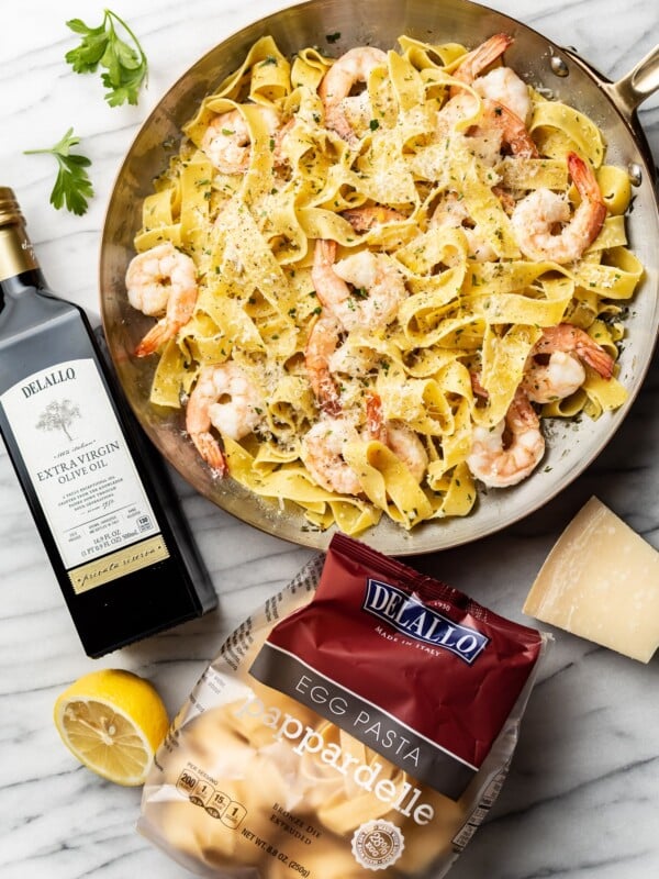 pappardelle with shrimp surrounded by a package of DeLallo's Egg Pappardelle and Private Reserve Olive Oil