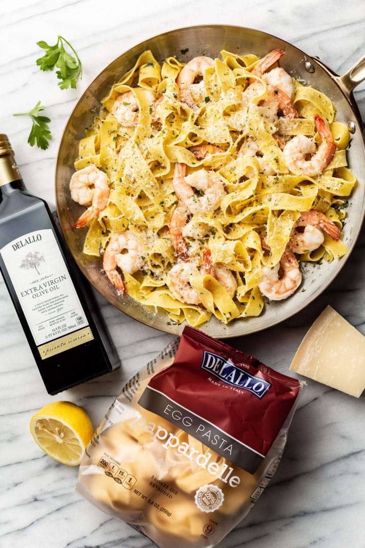 pappardelle with shrimp surrounded by a package of DeLallo's Egg Pappardelle and Private Reserve Olive Oil