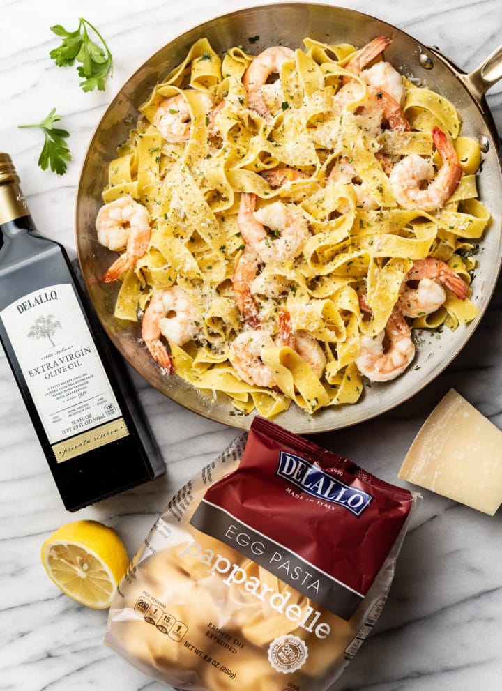 pappardelle with shrimp surrounded by a package of DeLallo's Egg Pappardelle and Private Reserve Olive Oil