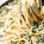 close-up of creamy spinach artichoke pasta being lifted up with tongs