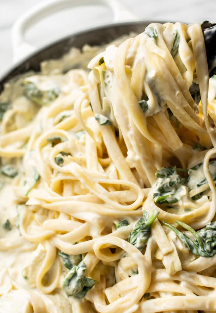 close-up of creamy spinach artichoke pasta being lifted up with tongs