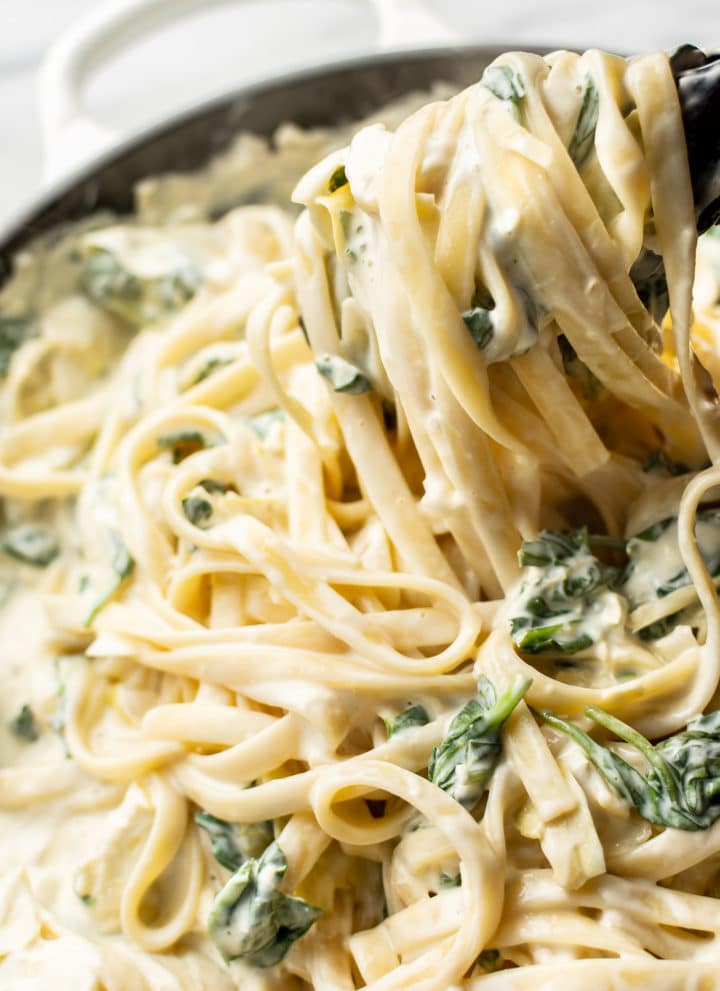 close-up of creamy spinach artichoke pasta being lifted up with tongs