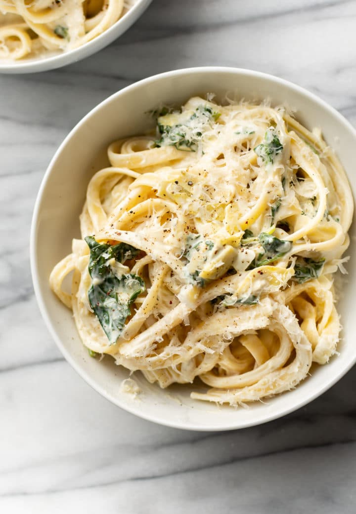 two white bowls with spinach and artichoke pasta