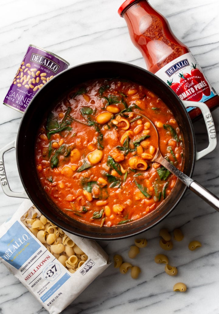 a pot full of bean and bacon soup pictured with DeLallo shellbows, passata, and cannellini beans