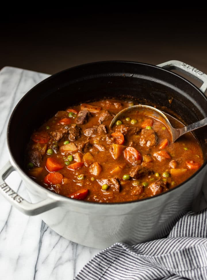 old fashioned beef stew in a Dutch oven with a ladle in the pot