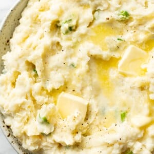 mashed potatoes with sour cream close-up in a serving bowl with butter pats on top