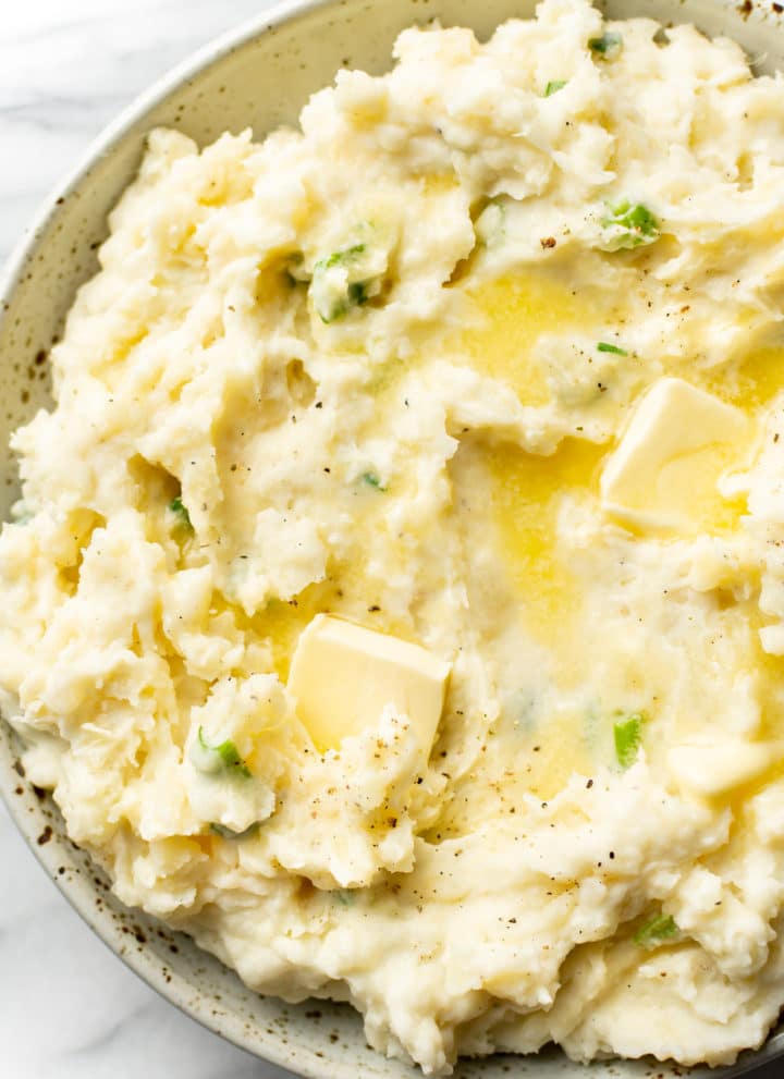 mashed potatoes with sour cream close-up in a serving bowl with butter pats on top