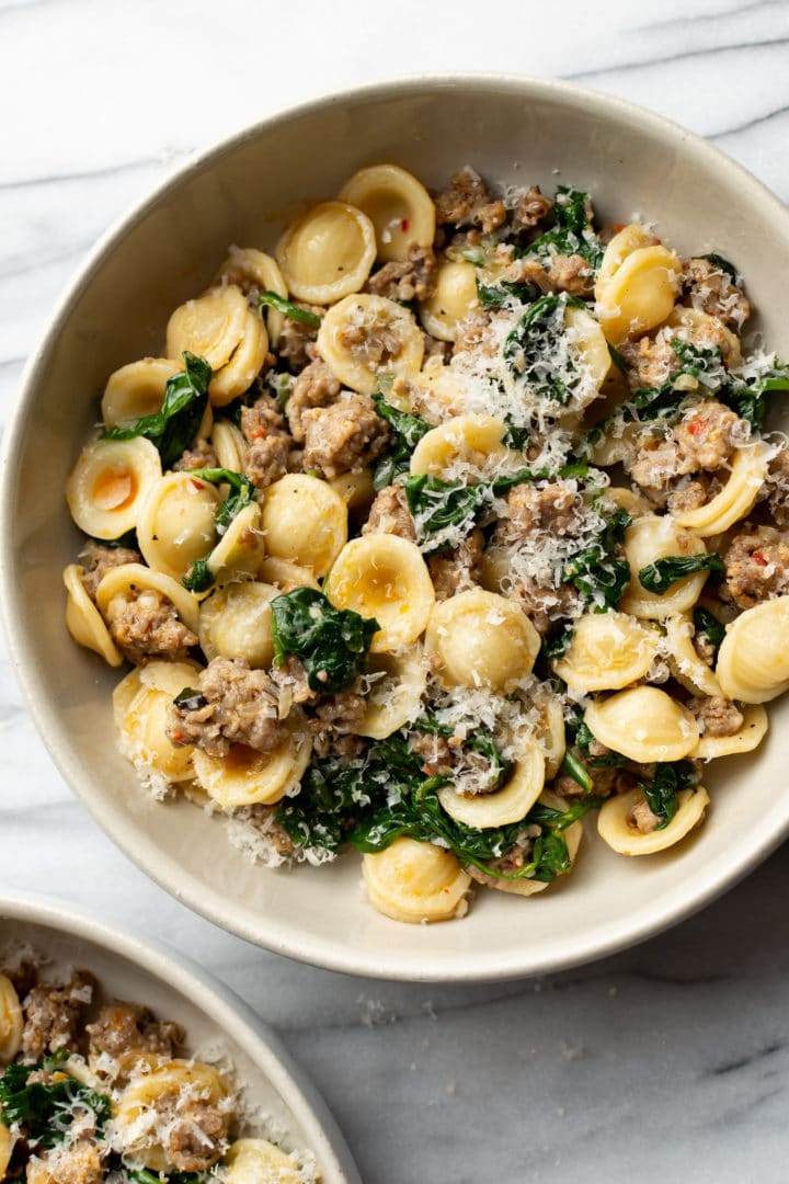 sausage and spinach orecchiette served in two beige bowls