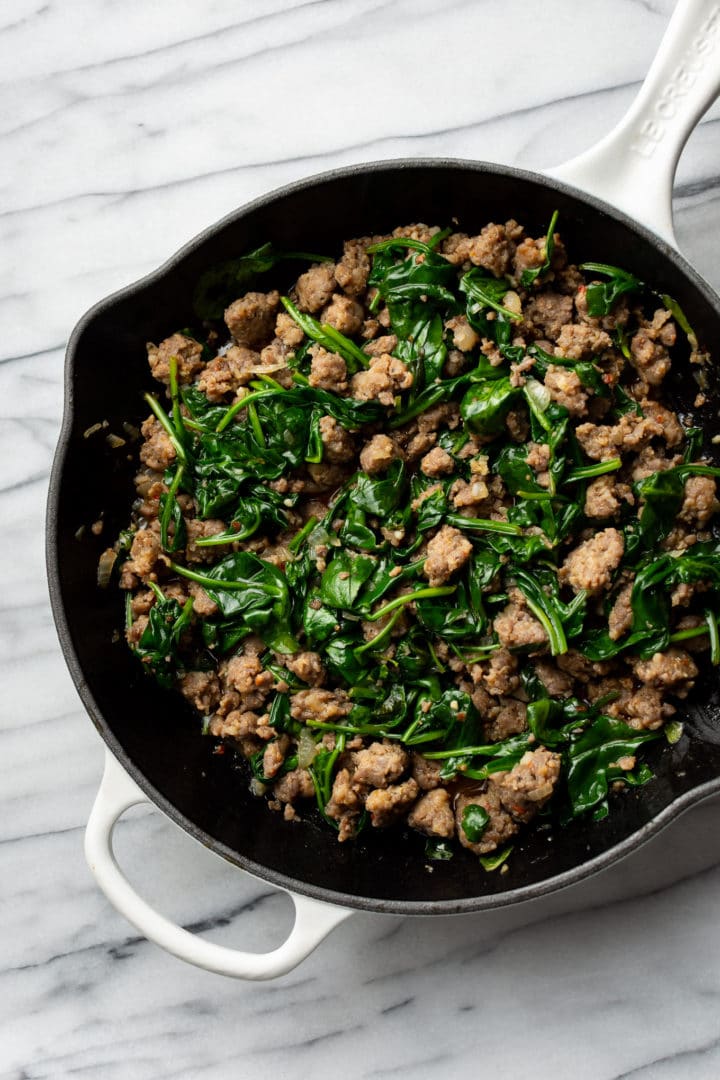 sausage and spinach sauce for orecchiette in a white cast iron skillet