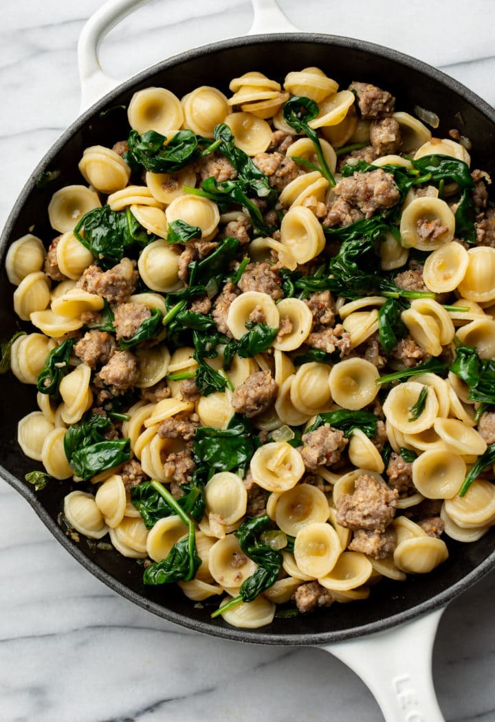 close-up of orecchiette with sausage and spinach sauce in a skillet