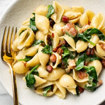 brie pasta with spinach and pancetta in a white bowl with a golden fork
