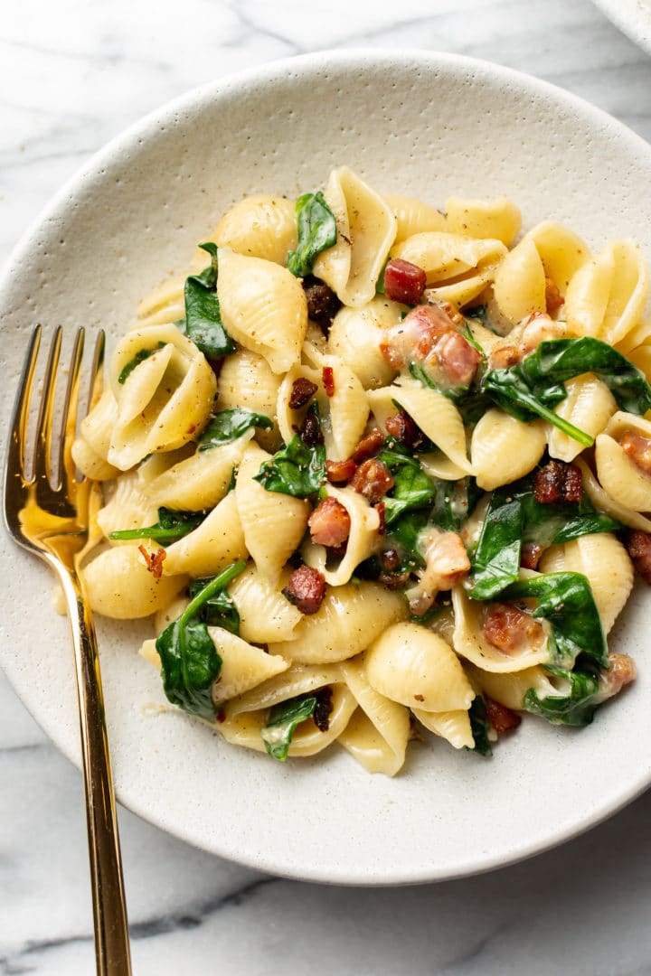 brie pasta with spinach and pancetta in a white bowl with a golden fork