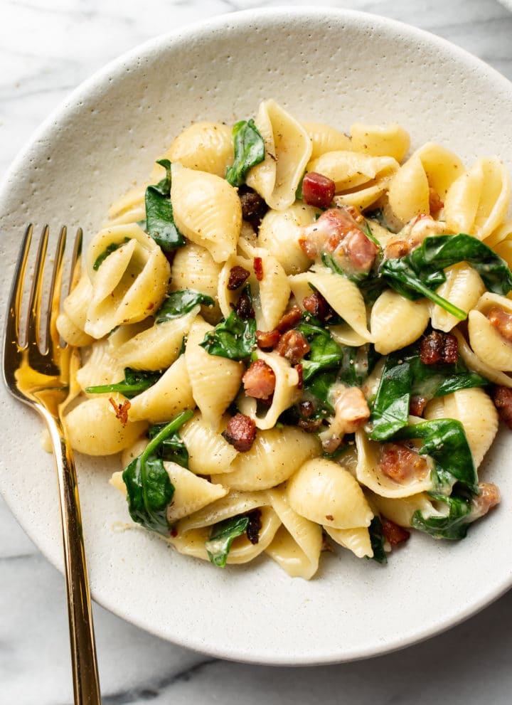 brie pasta with spinach and pancetta in a white bowl with a golden fork