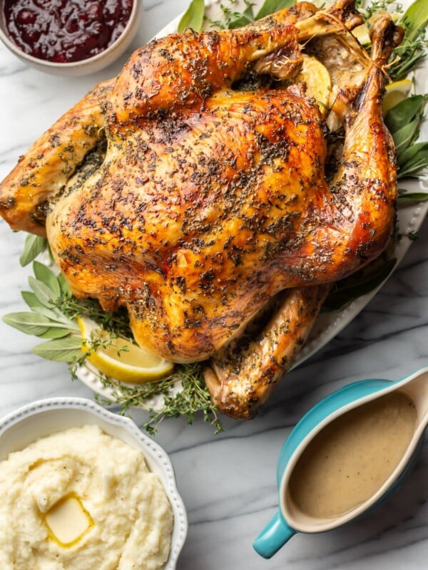 roast turkey on a marble background with a bowl of mashed potatoes, cranberry sauce, and a gravy boat