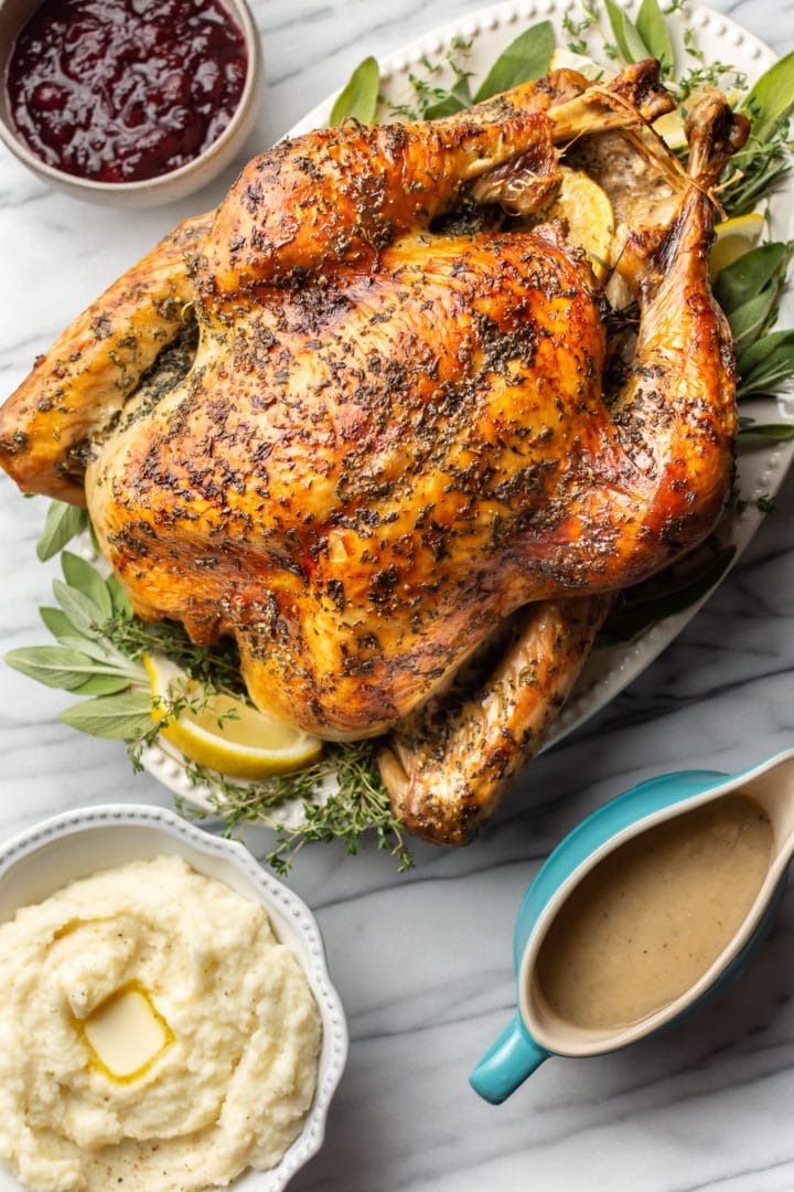 roast turkey on a marble background with a bowl of mashed potatoes, cranberry sauce, and a gravy boat