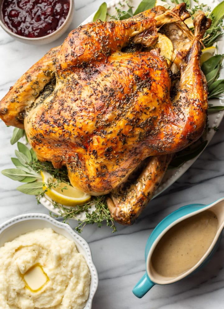 roast turkey on a marble background with a bowl of mashed potatoes, cranberry sauce, and a gravy boat