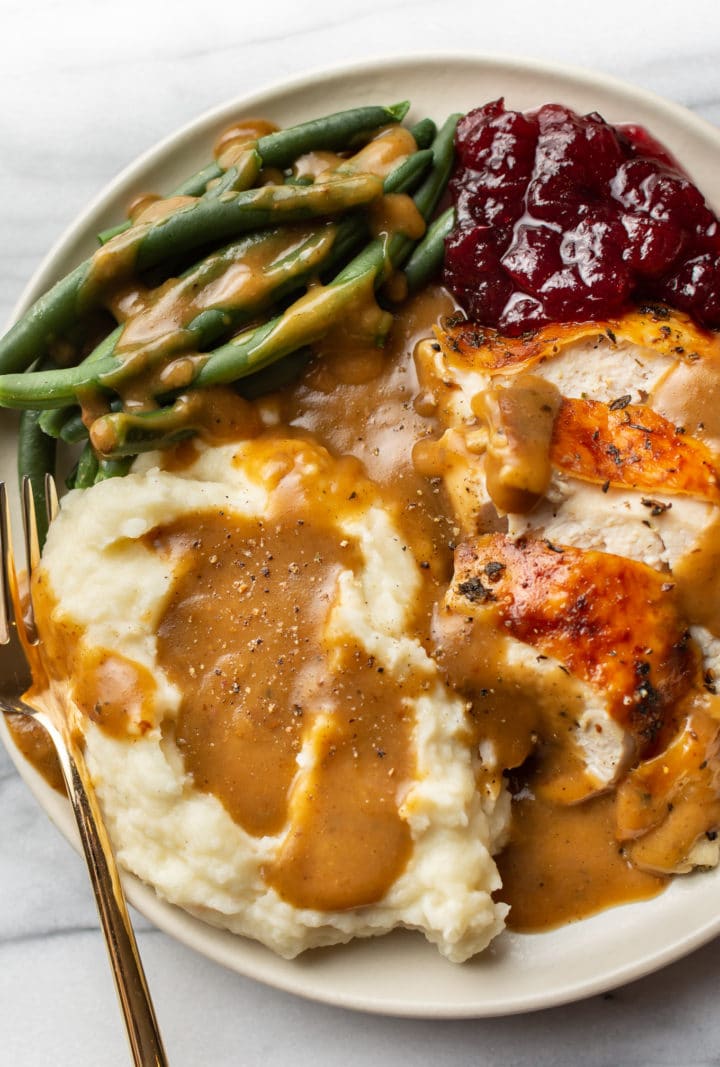 Thanksgiving dinner on a plate with sliced roasted turkey, mashed potatoes, gravy, green beans, and cranberry sauce